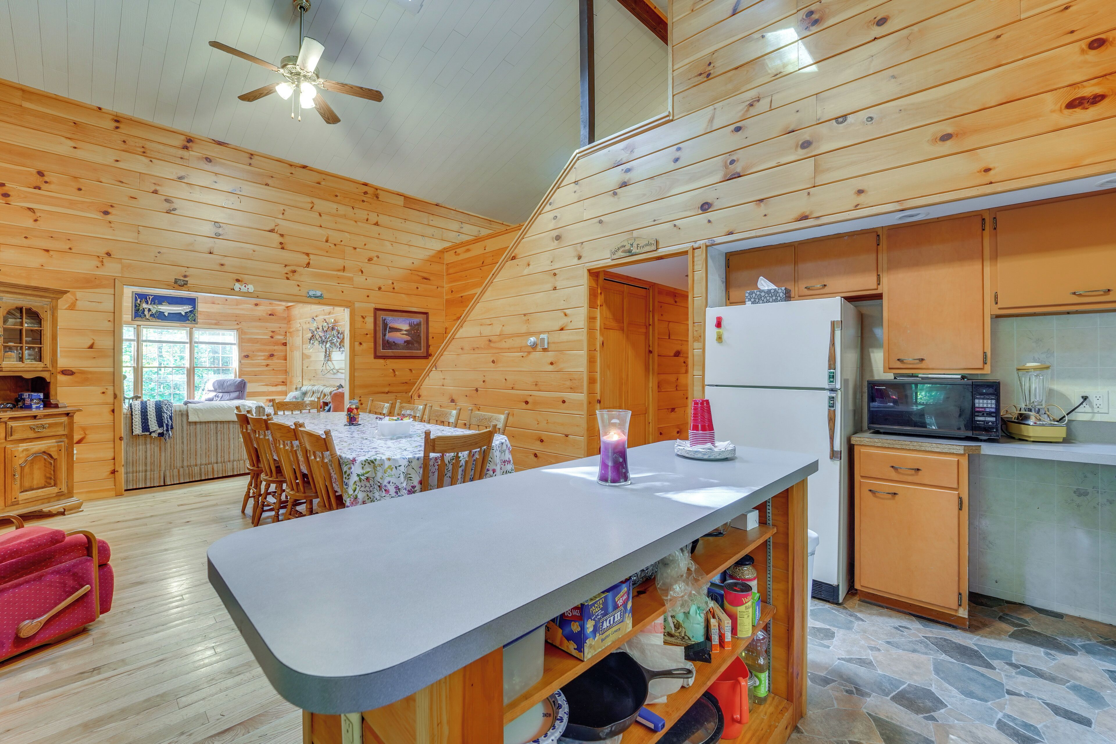 A wooden cabin interior with a dining area, kitchen, and a staircase.
