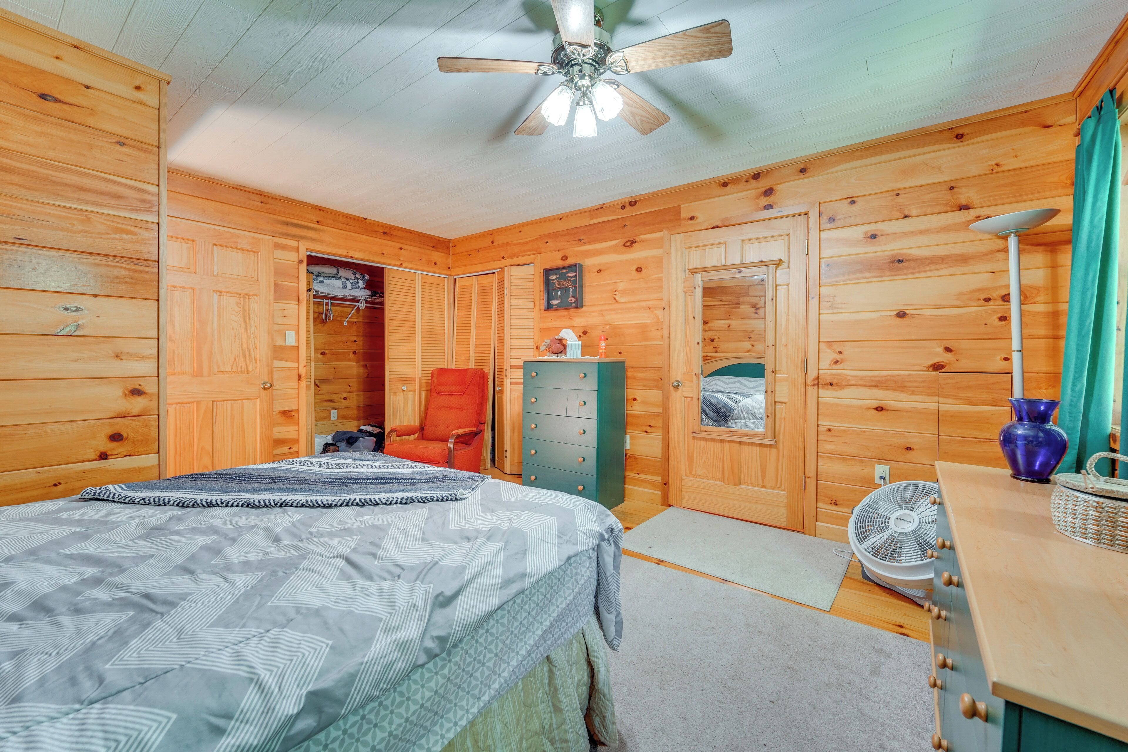 A wooden cabin bedroom with a bed, a dresser, a chair, a fan, and a ceiling fan.