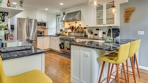 Una cocina moderna con armarios blancos, electrodomésticos de acero inoxidable y una isla central con taburetes de bar.