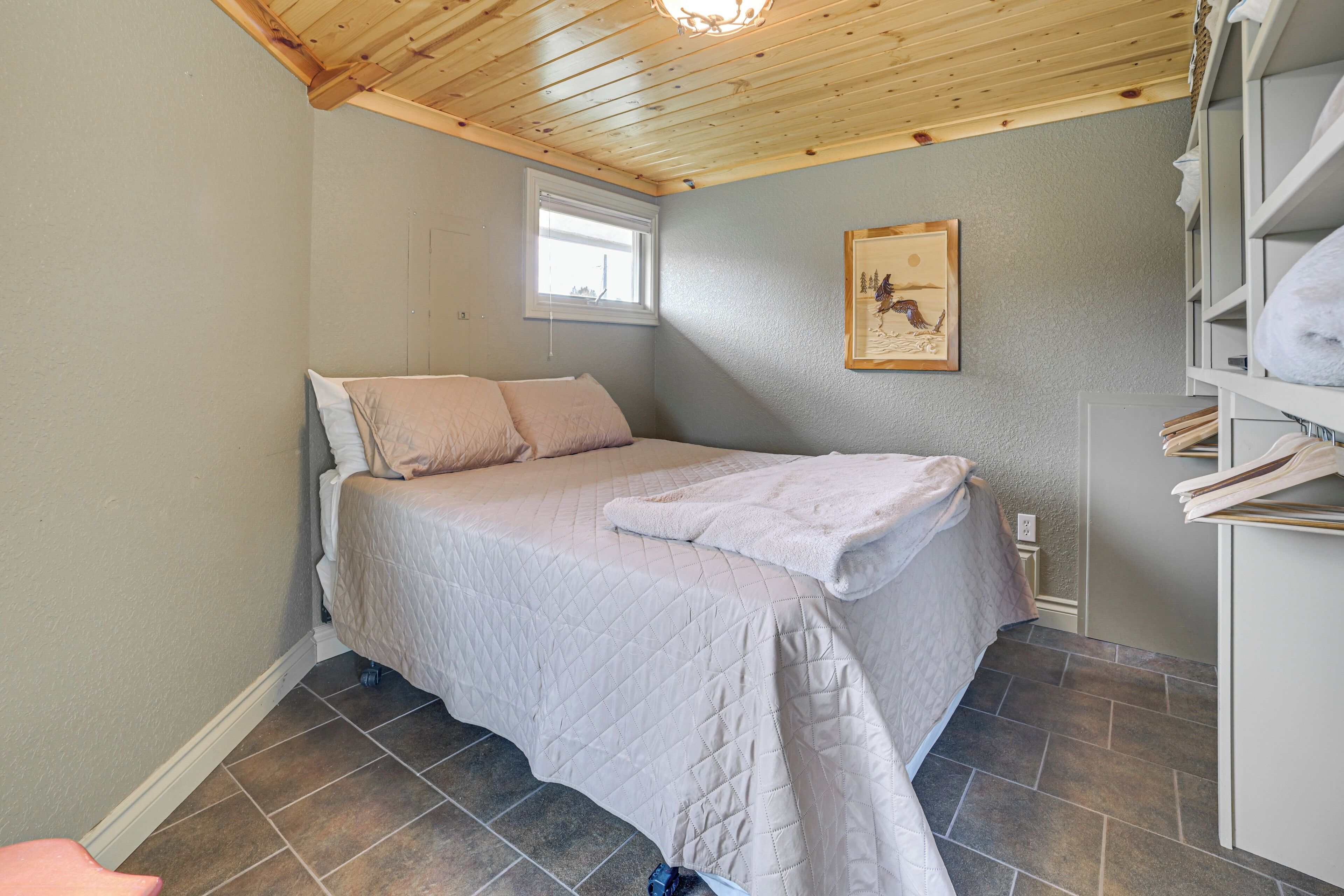 A bedroom with a bed, a window, a painting, and a shelf with towels.