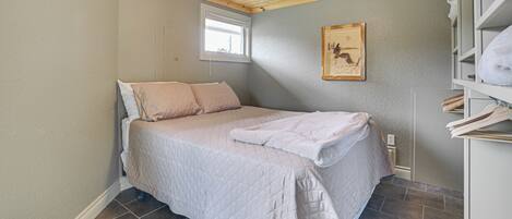 A bedroom with a bed, a window, a painting, and a shelf with towels.