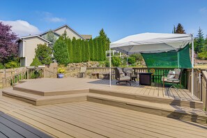 Une terrasse en bois avec des meubles d’extérieur, un auvent blanc et une vue sur une maison et des arbres.