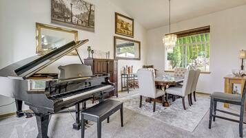 A grand piano in a spacious living room with a dining area, large windows, and artwork on the walls.