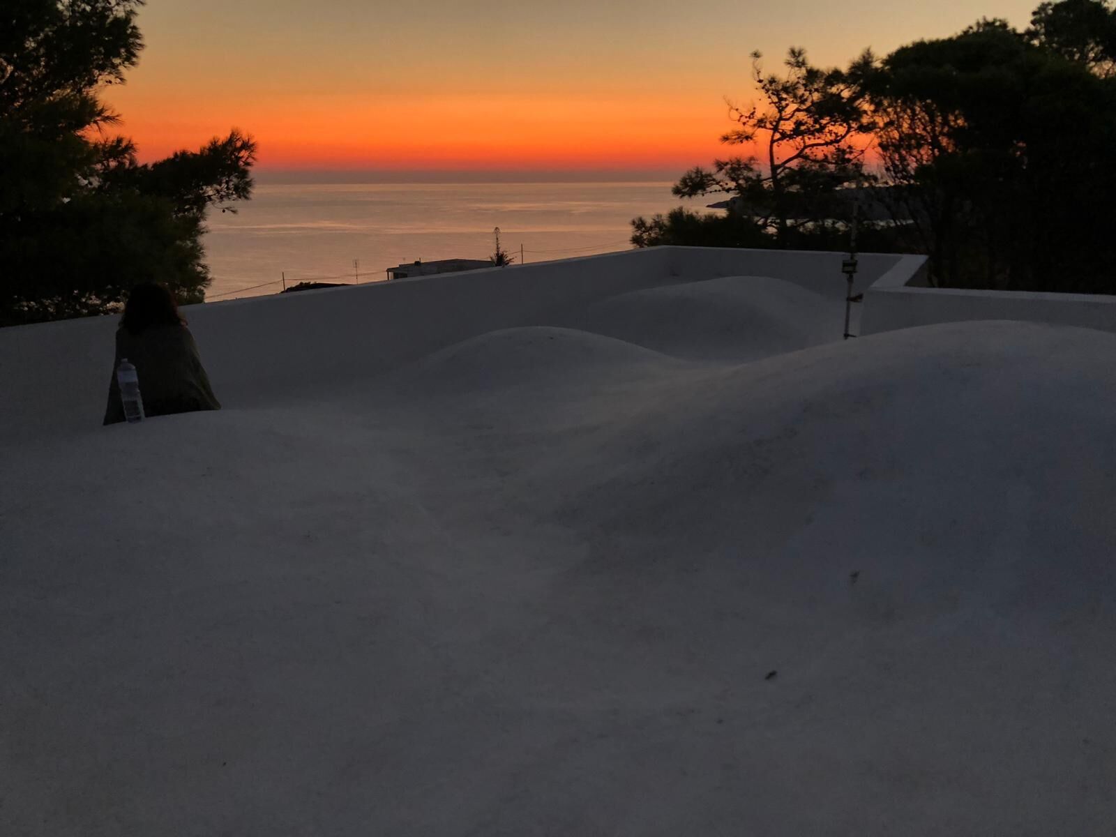 A desert landscape with undulating sand dunes and a sunset over the ocean.