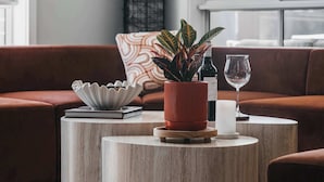 Una sala de estar moderna con un sofá de cuero marrón, dos mesas redondas de madera, una planta en maceta, una copa de vino y una vela.