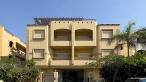 A multi-story building with balconies, a gated entrance, and solar panels on the roof. - Kennah Chill & Swim | 2BR with Pool, October City (6th of October City)