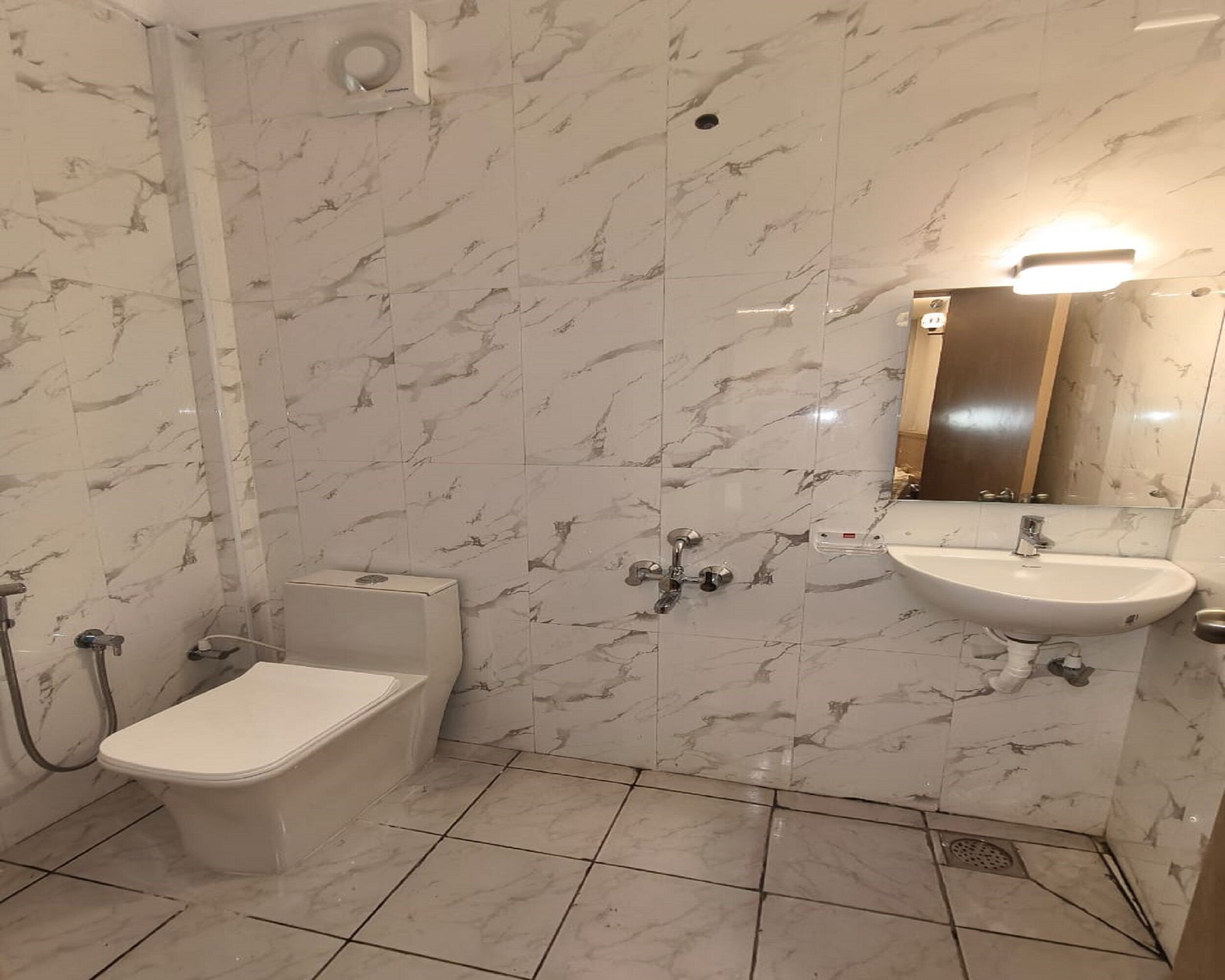 Et badeværelse med toilet, bidet og vask, alt sammen med marmorvægge og gulvfliser.