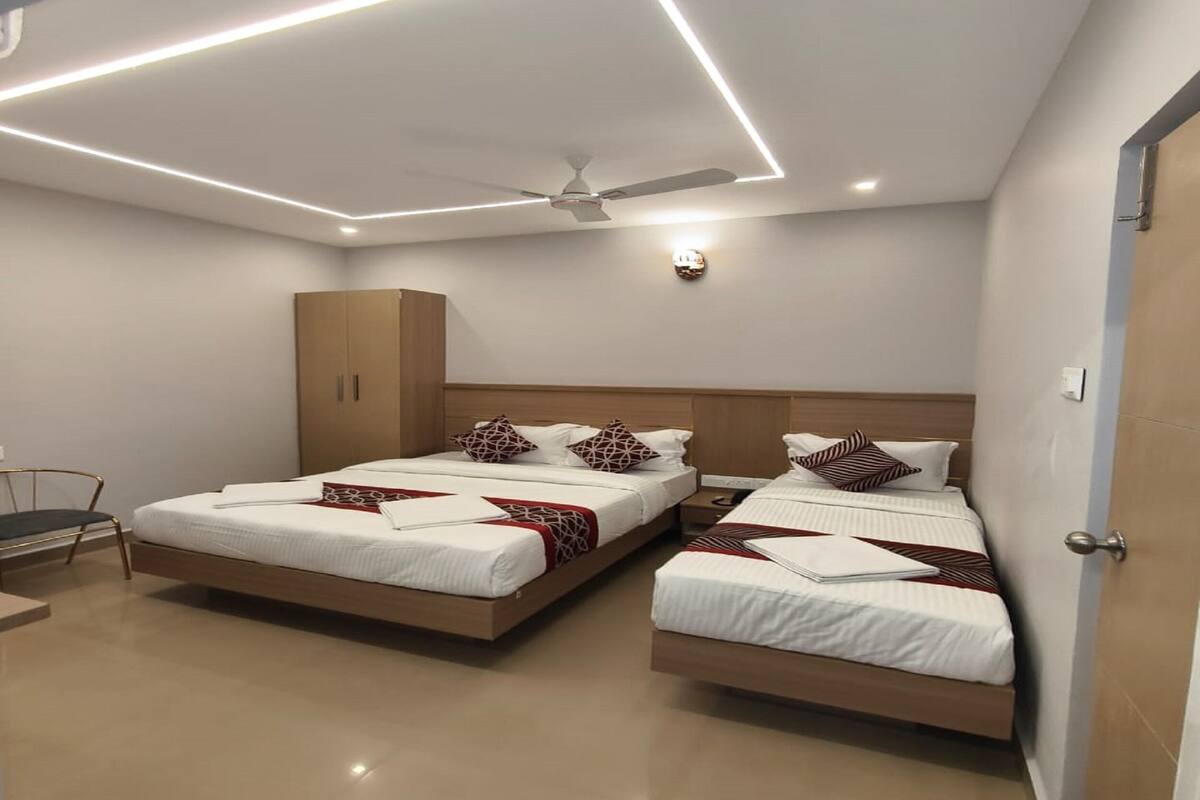 A modern hotel room with two beds, a wardrobe, a ceiling fan, and recessed lighting.