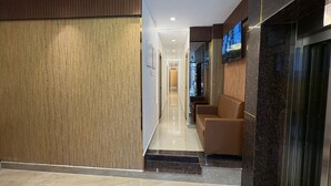 A modern hotel lobby with a wooden panel wall, a seating area with leather chairs, and a reception desk.