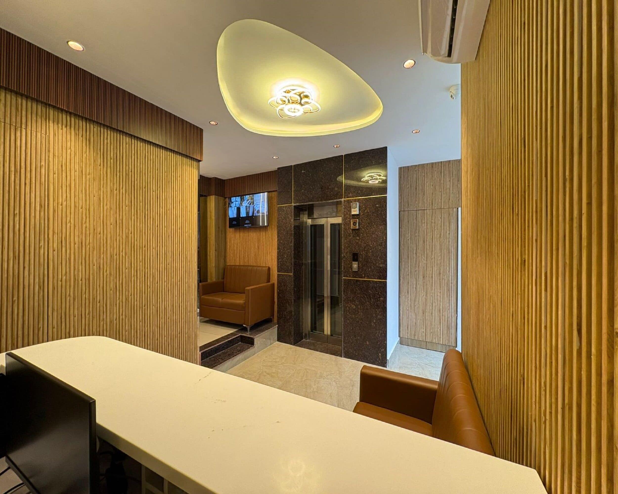 A modern hotel lobby with a reception desk, seating area, and a television screen.