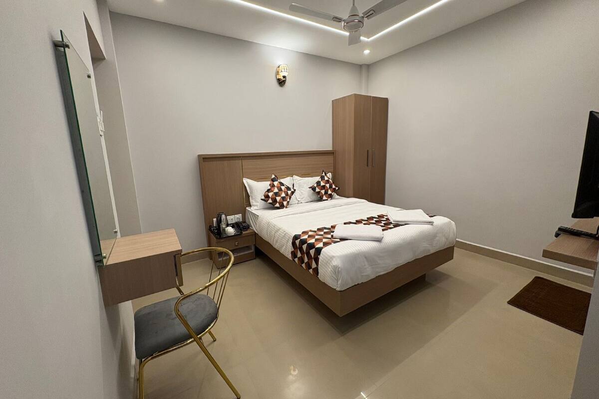 A modern hotel room with a large bed, a desk, a chair, a wardrobe, and a television.
