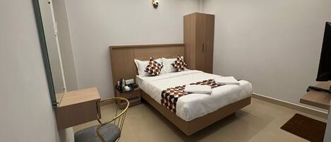 Una habitación de hotel moderna con una cama grande, un escritorio, una silla, un armario y un televisor.