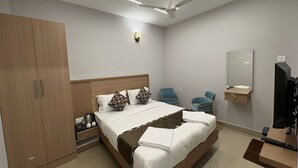 A modern bedroom with a large bed, two chairs, a wardrobe, a mirror, and a TV.