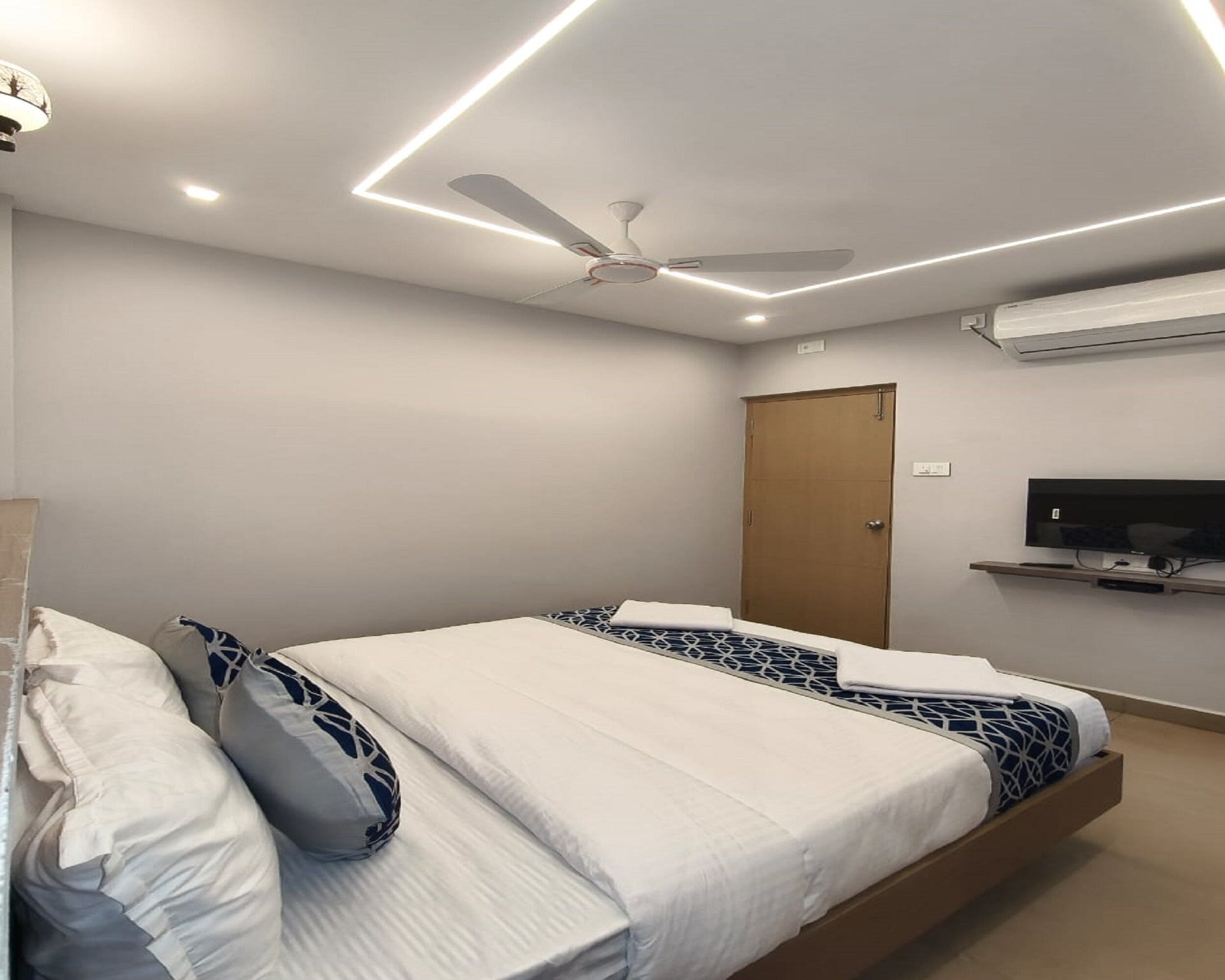 Une chambre moderne avec un lit, un ventilateur de plafond et un téléviseur fixé au mur.