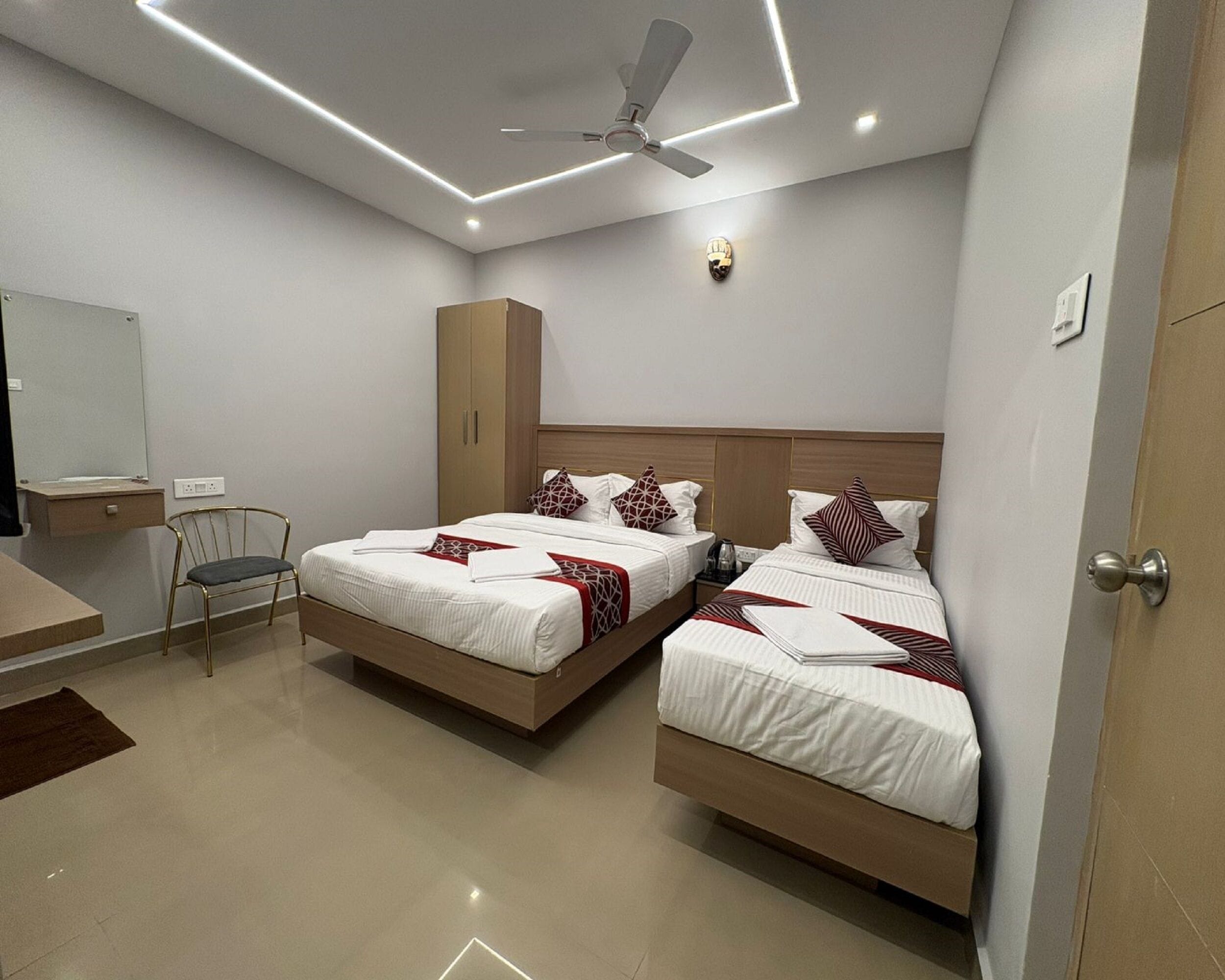A modern hotel room with two single beds, a desk, a chair, a wardrobe, and a ceiling fan.