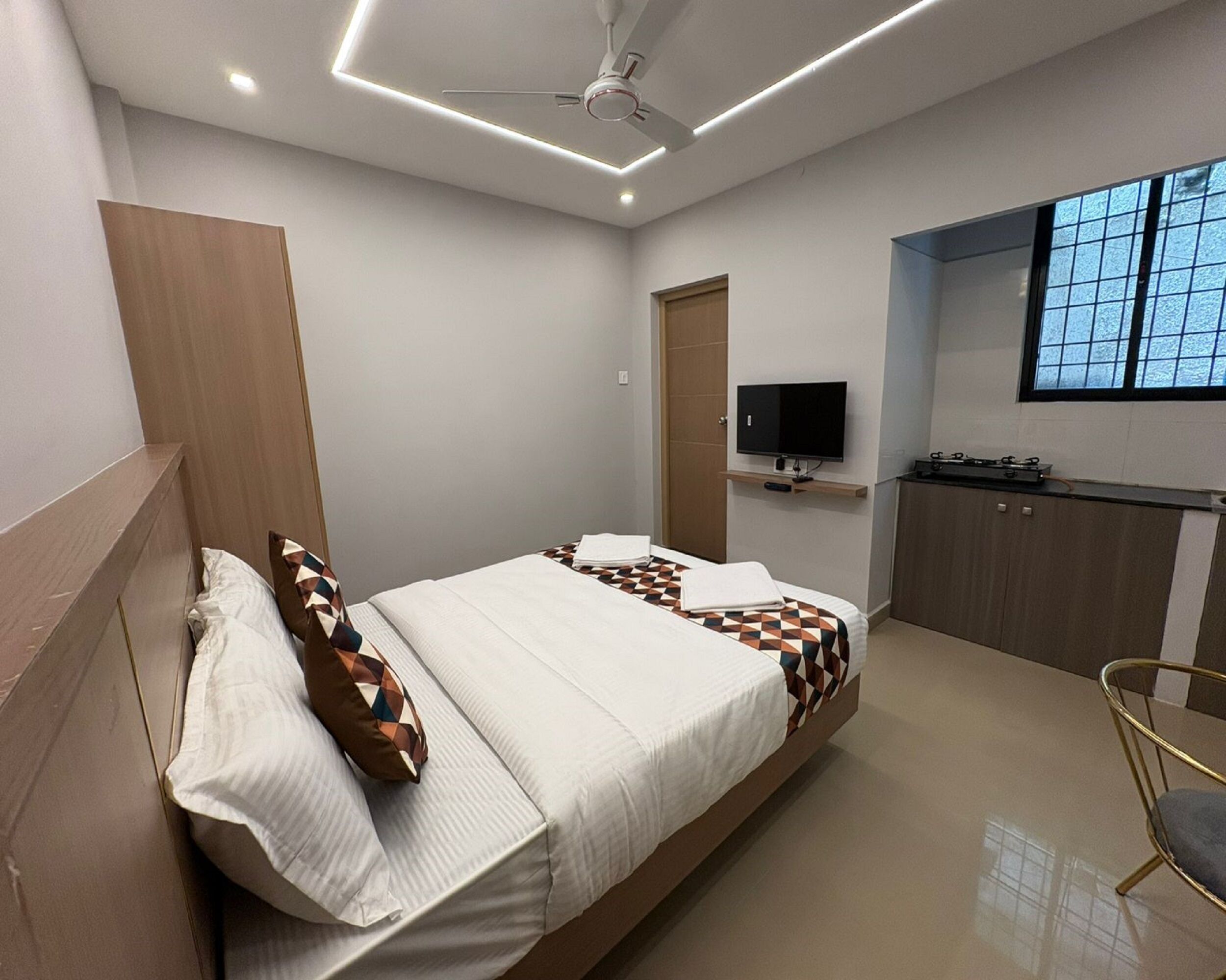 Un dormitorio moderno con cama, televisión, kitchenette y ventana.