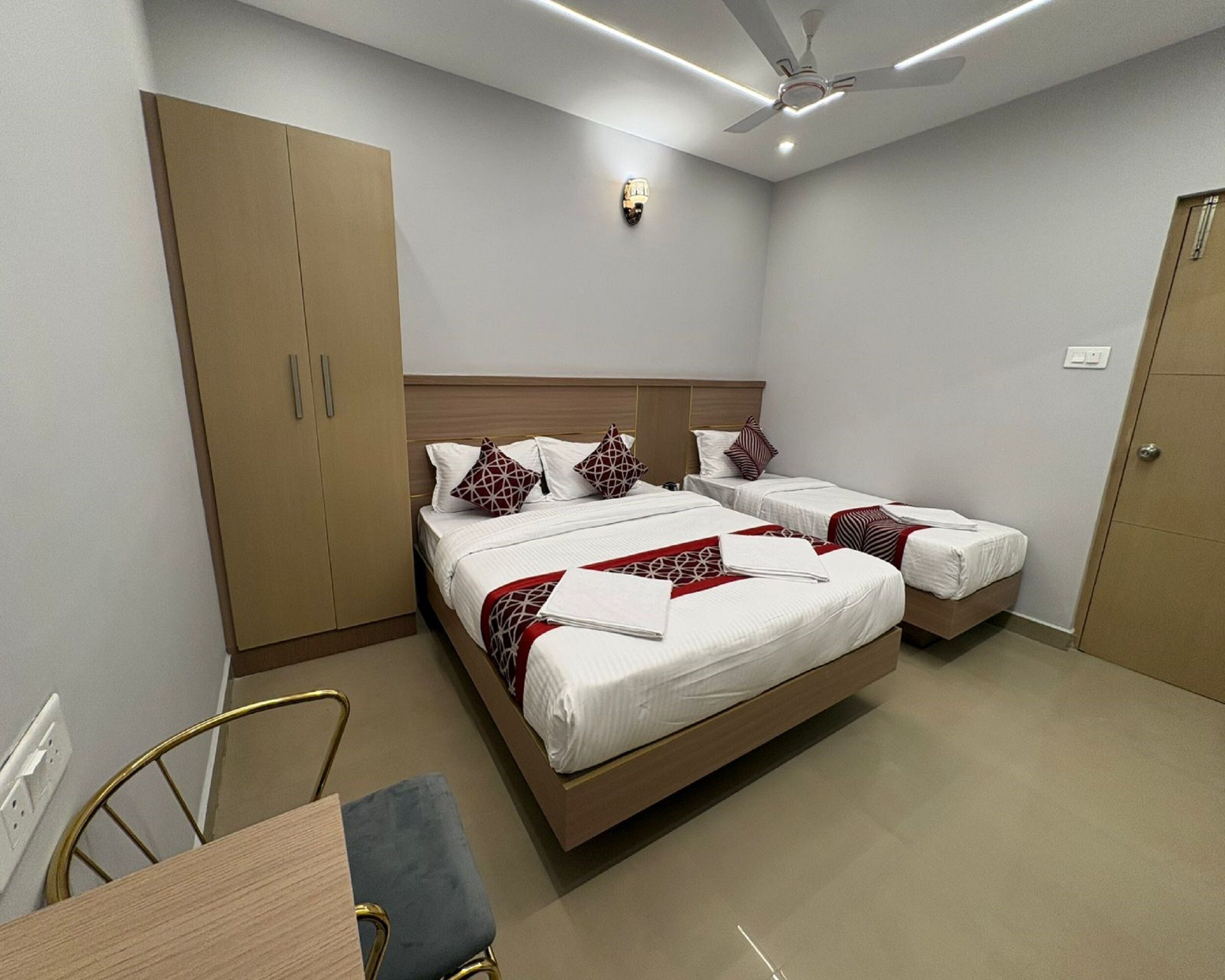 A hotel room with two beds, a wardrobe, a desk with a chair, and a ceiling fan.