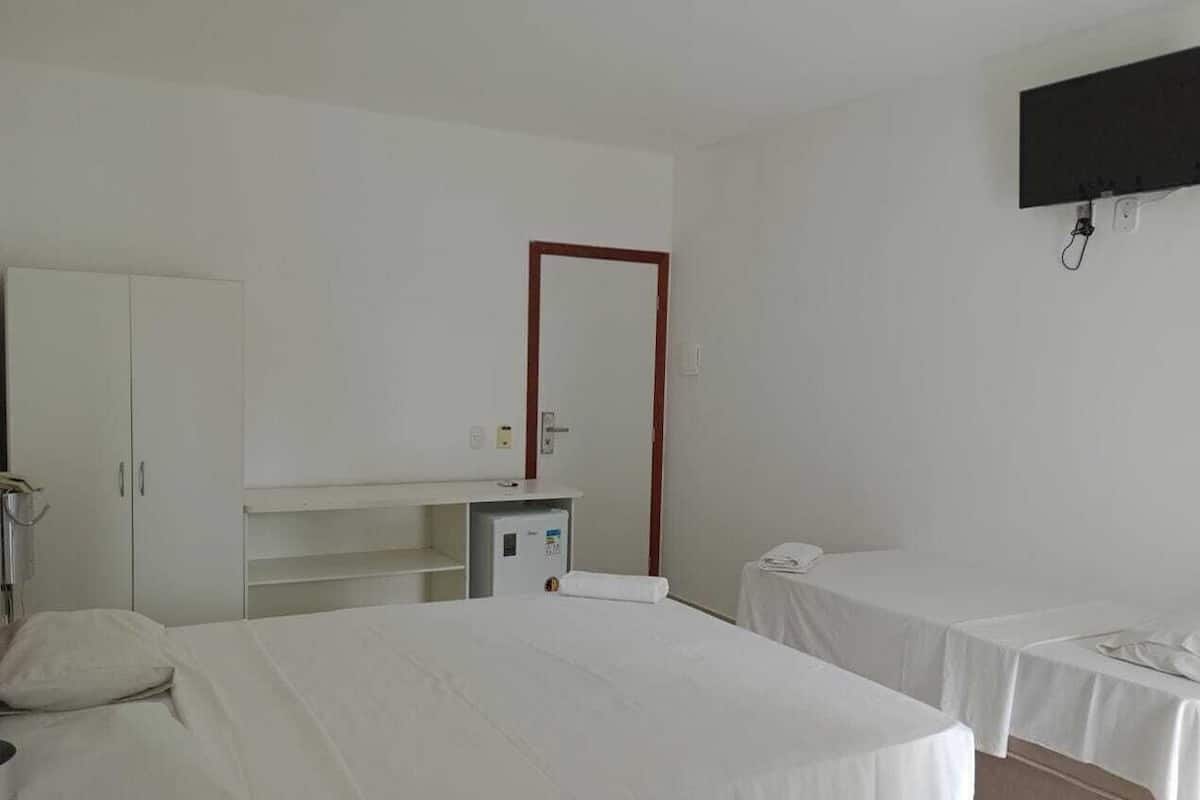 Hotellihuone, jossa on sänky, kaksi yöpöytää, vaatekaappi, työpöytä tuolilla, peili ja seinälle asennettu televisio.