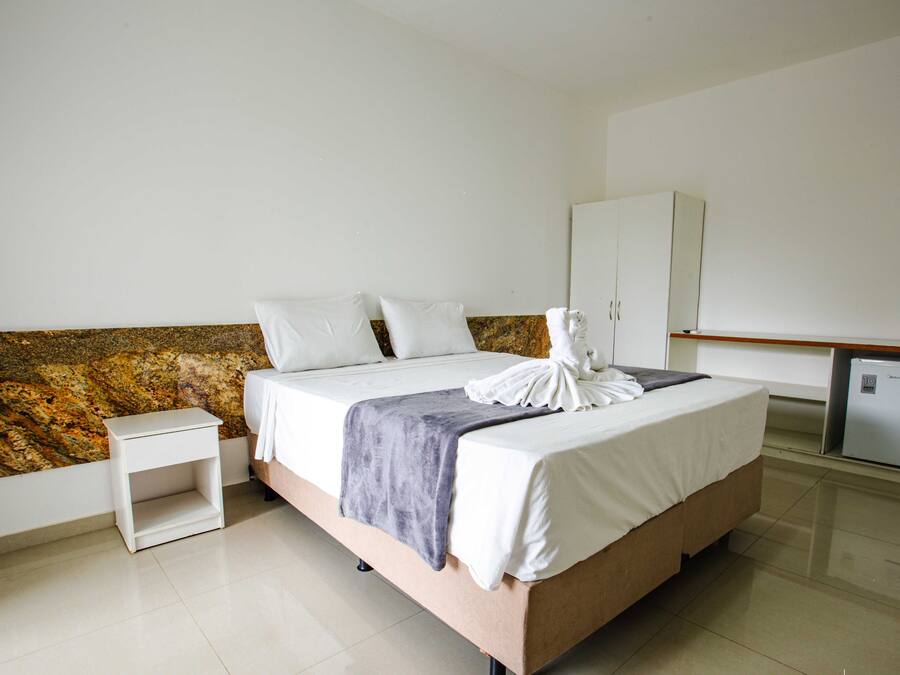 Quarto de hotel com cama, mesa de cabeceira, guarda-roupa e minibar.