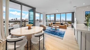 Een moderne woonkamer met een ronde tafel, twee stoelen, een bank en uitzicht op de stad door grote ramen.