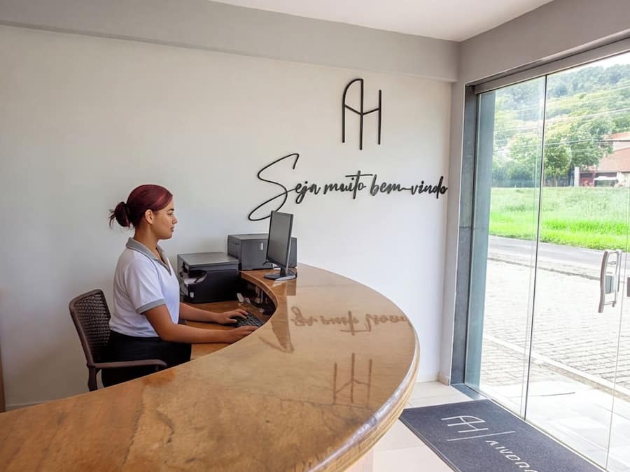 A reception desk with a receptionist, a computer, and a wall sign with text.