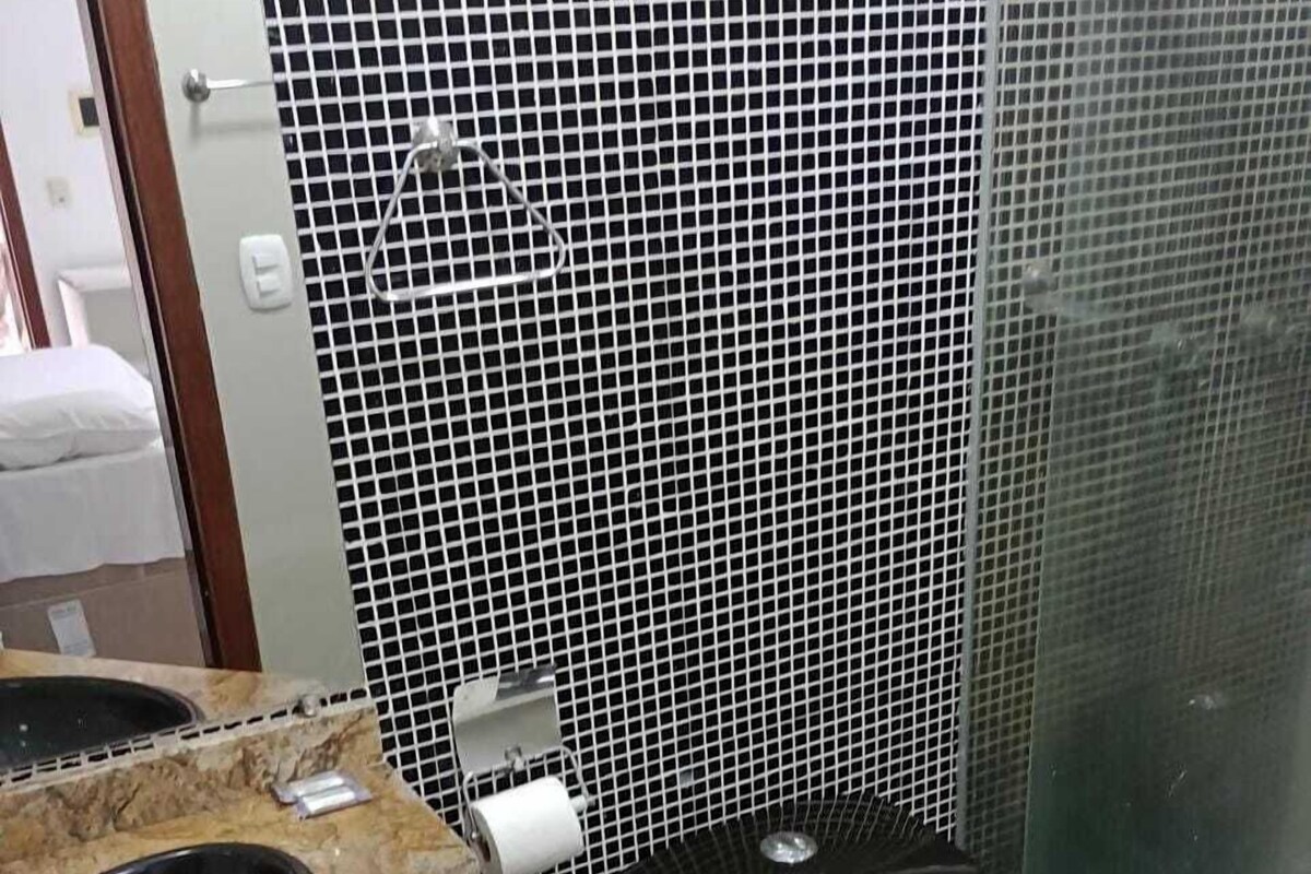 A bathroom with a black toilet, a sink with a marble countertop, and a trash bin.