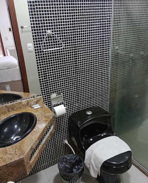 A bathroom with a black toilet, a sink with a marble countertop, and a trash bin. - Rede Andrade Porto Seguro (Porto Seguro)