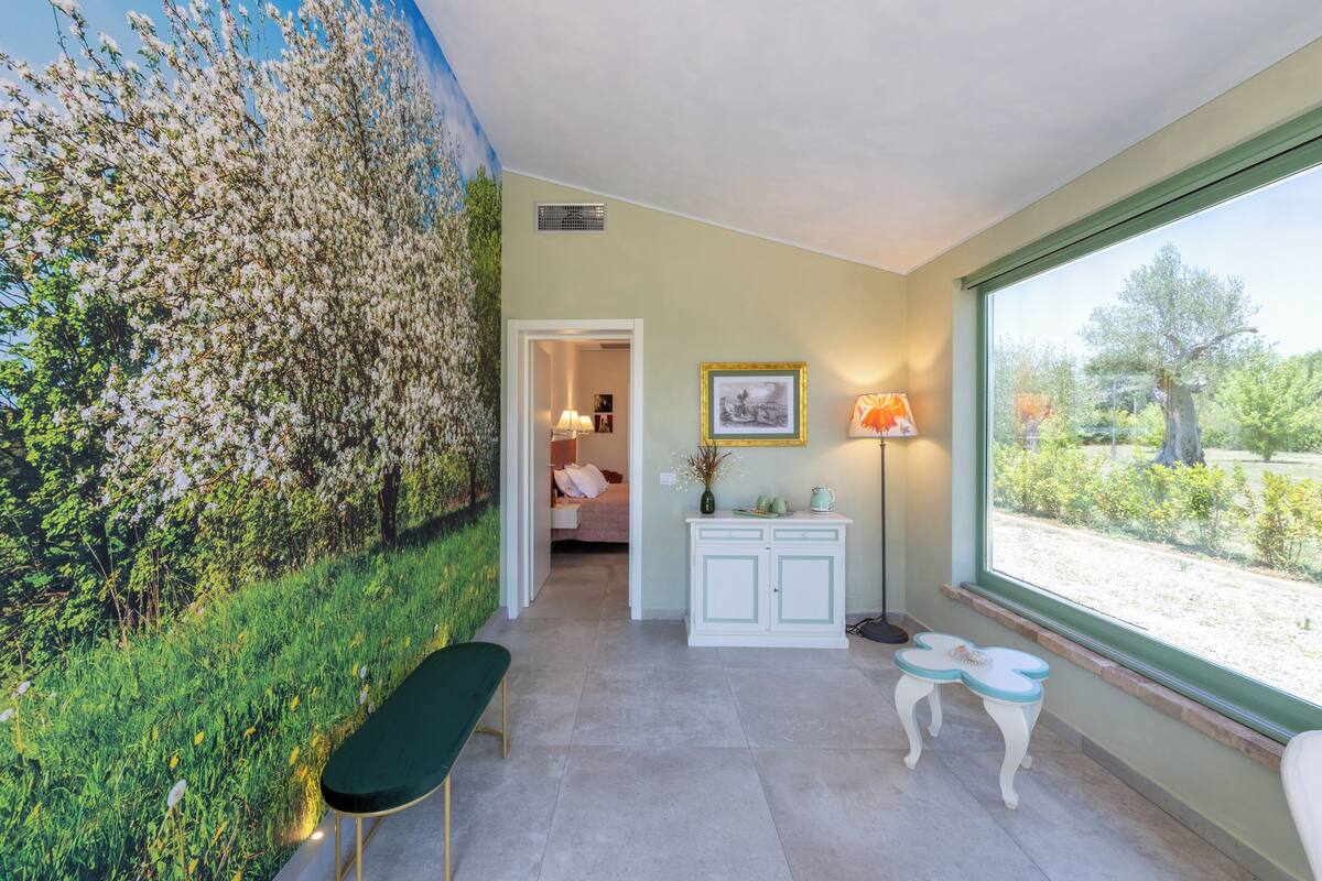 A room with a large window, a green bench, a small table, and a cabinet.