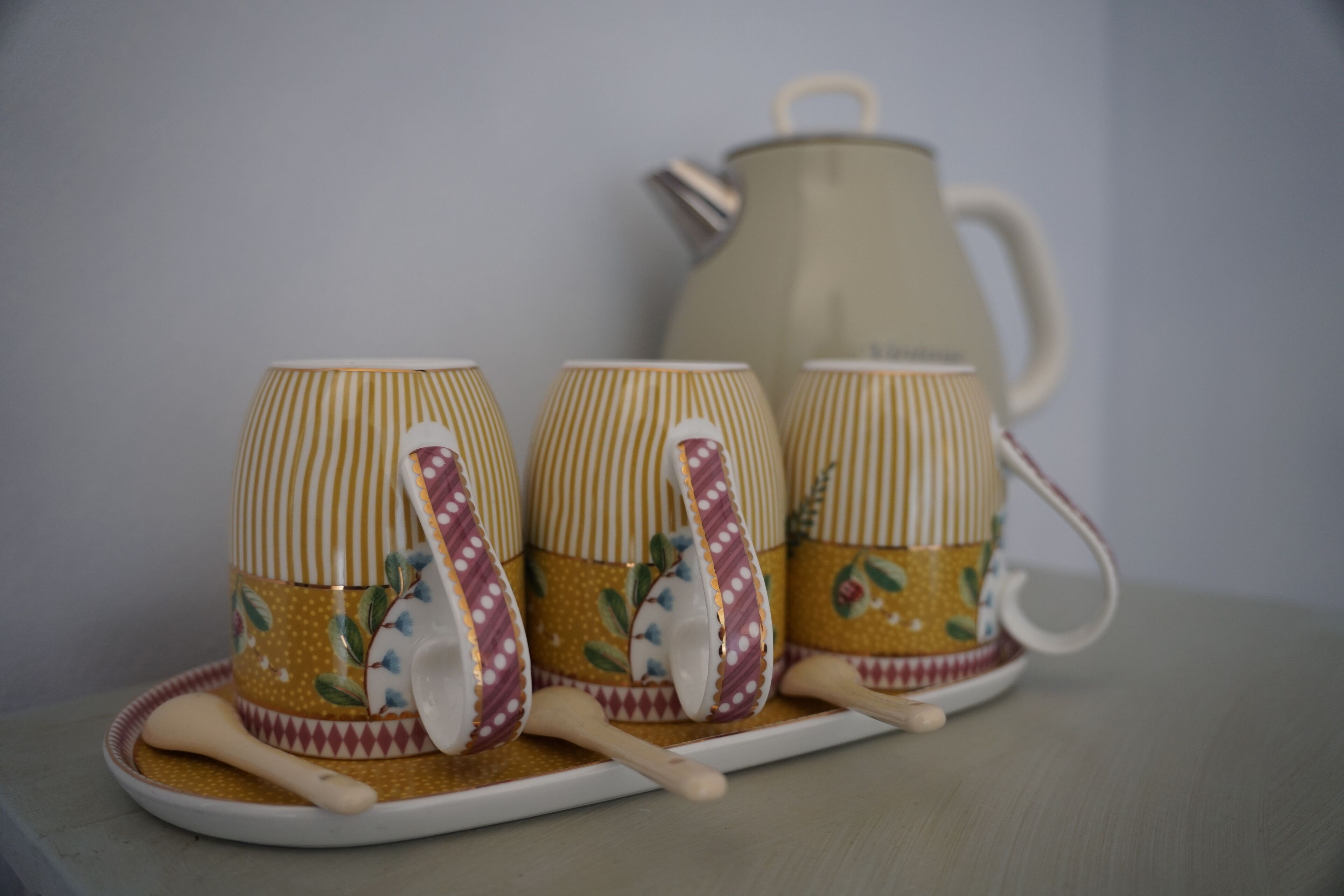 Three striped cups with floral designs on a tray, accompanied by a teapot.