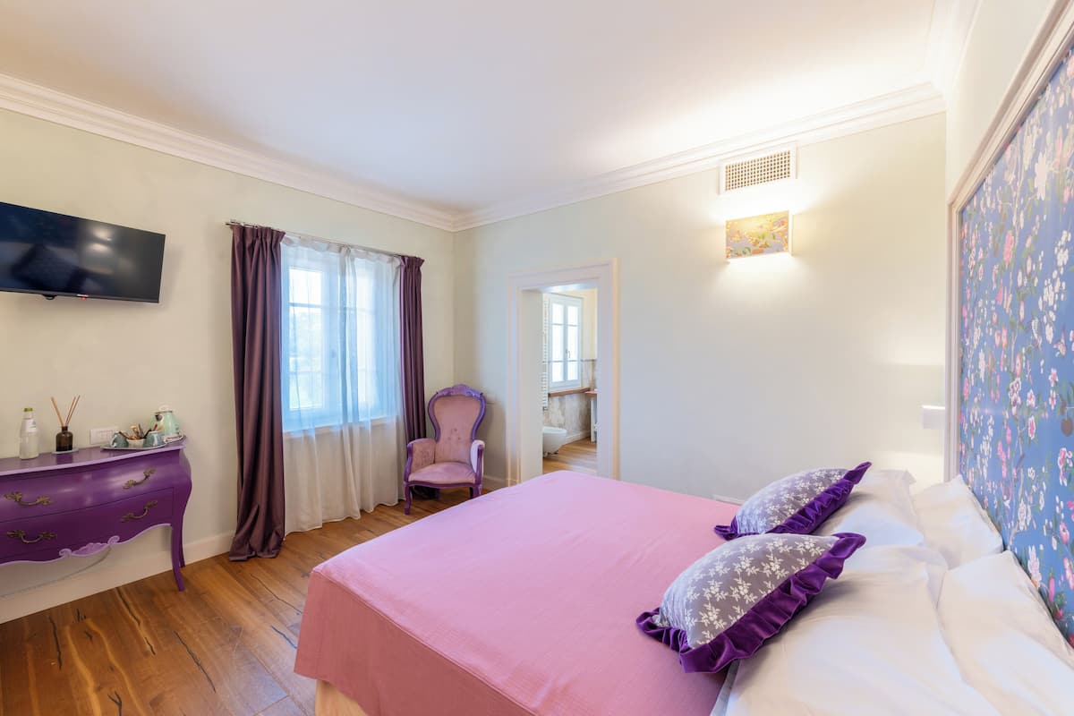 A bedroom with a bed, a dresser, a chair, a television, and a bathroom visible through an open door.