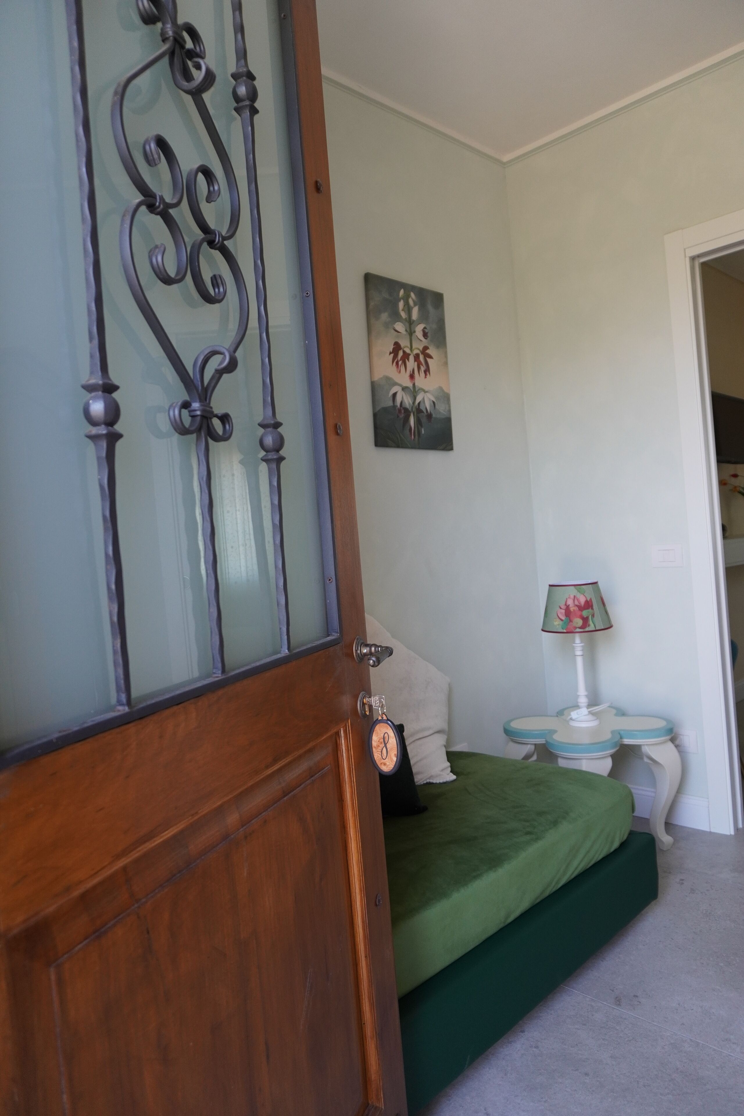 Una camera da letto con un letto verde, una porta in legno con pannelli di vetro, un quadro appeso al muro e una lampada sul comodino.