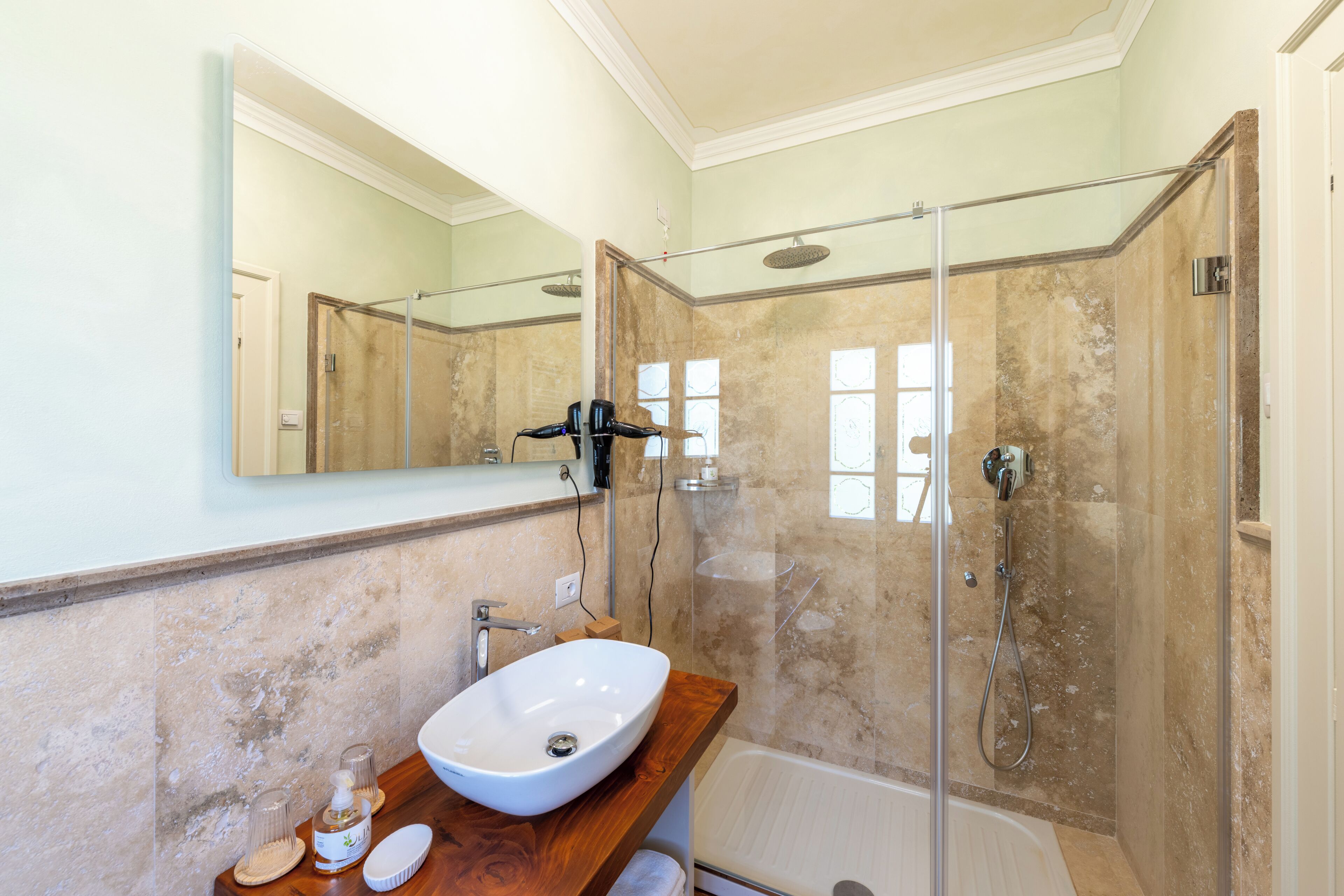Ein Badezimmer mit einem großen Spiegel, einem weißen Waschbecken, einer Holzkommode, einer Duschkabine aus Glas und einer Badewanne.