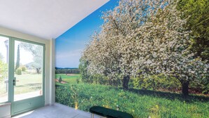 Una habitación con un ventanal amplio, una banca y un mural de un árbol con flores blancas.
