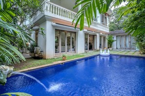 A poolside view of a two-story house with a large pool, surrounded by lush greenery and potted plants. - 4bhk Villa in Siolim Pool Lush Forest View (Siolim)