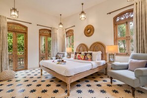A bedroom with a large bed, two bedside tables, a chair, and a window with curtains. - 4bhk Villa in Siolim Pool Lush Forest View (Siolim)