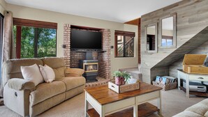 A living room with a brick fireplace, a flat-screen TV, a sofa, and a coffee table. - Game Room + Bar + Lake Views | Gated Marina + Mini Golf | Naci Lakeview Retreat (Bradley)