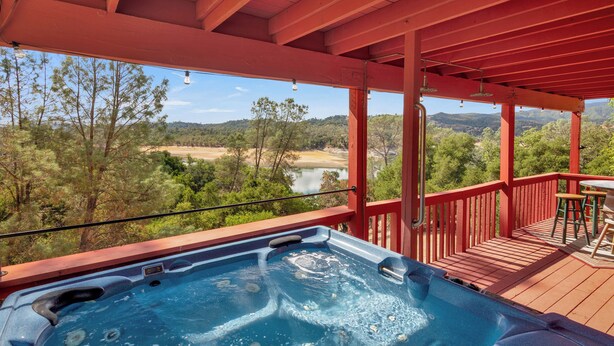 A hot tub on a wooden deck with a view of a river and forest. - Game Room + Bar + Lake Views | Gated Marina + Mini Golf | Naci Lakeview Retreat (Bradley)