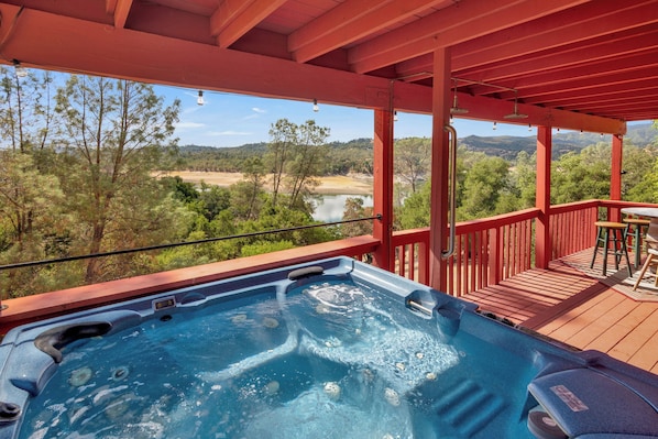 A hot tub on a wooden deck with a view of a river and forest.