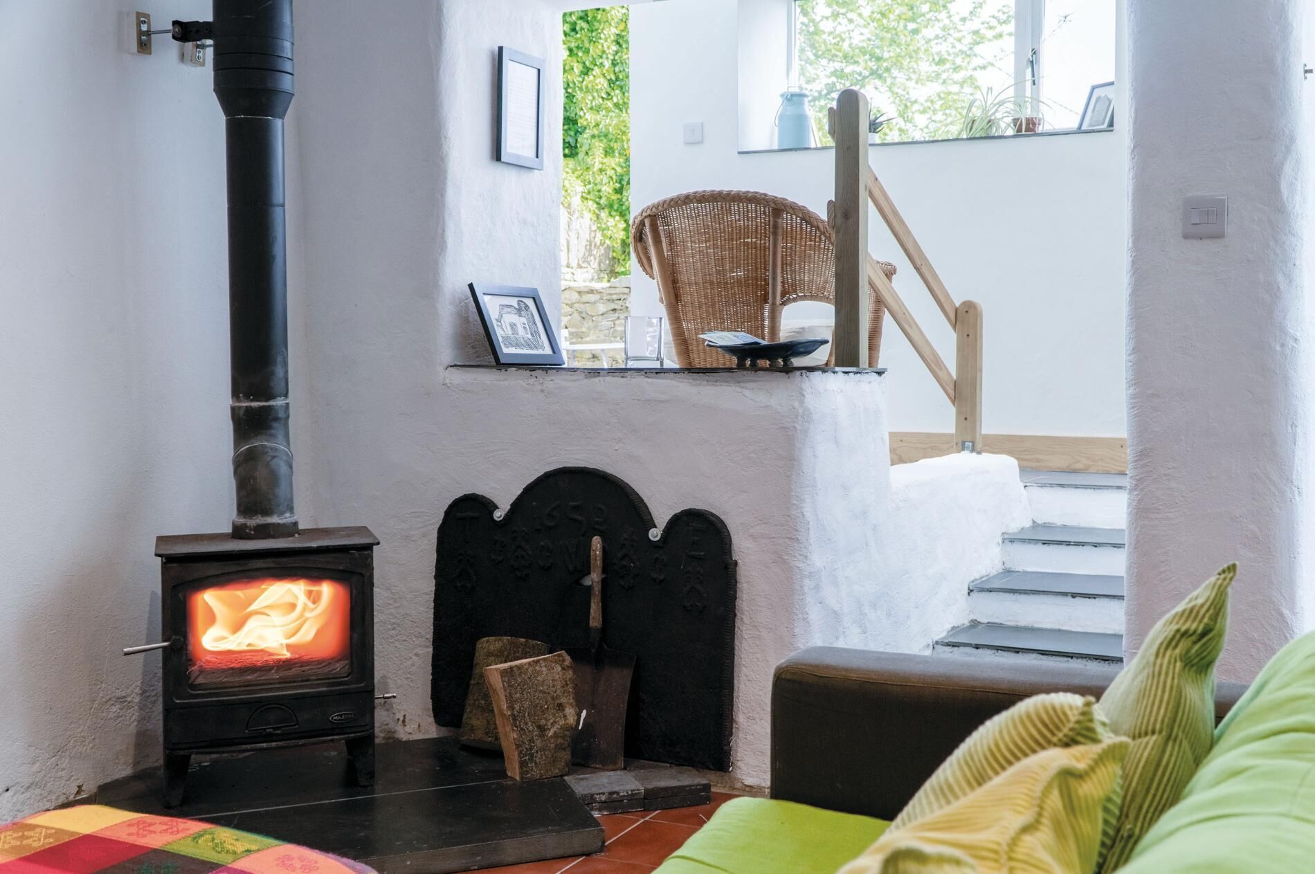 A cozy room with a wood-burning stove, a wicker chair, and a staircase leading to an upper level.