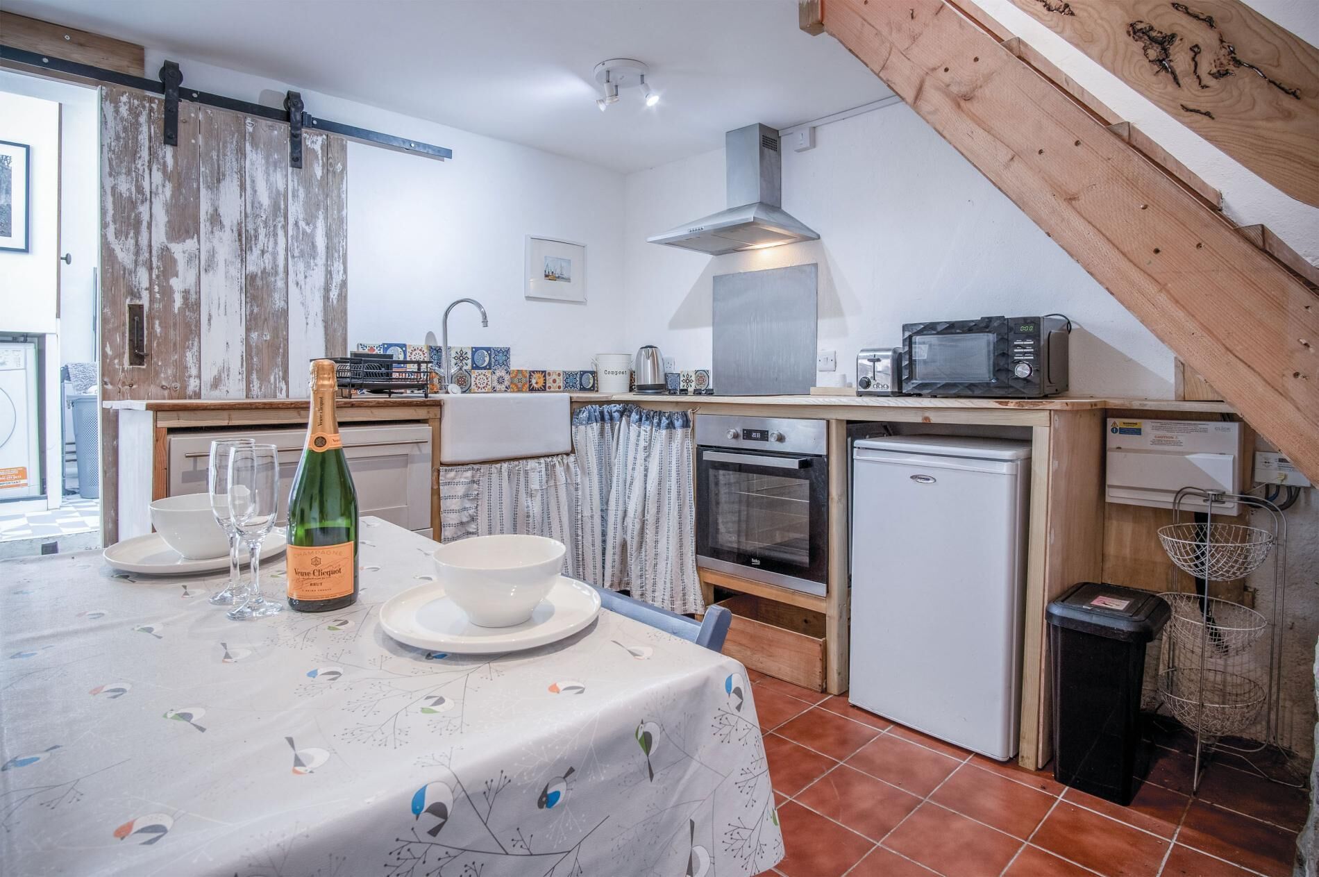 A compact kitchen with a dining area, featuring a table set with a bottle, glasses, and a bowl.