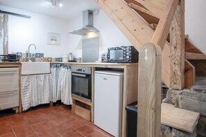 A compact kitchen with a built-in oven, a small refrigerator, and a microwave. There's a wooden staircase leading to an upper level. - Soap Barn - 1 Bedroom Cottage - Manorbier (Tenby)