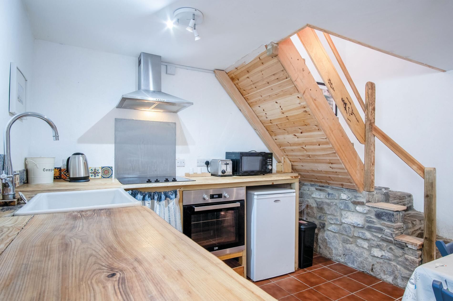 A compact kitchen with a wooden countertop, a stainless steel range hood, a microwave, a toaster, and a small refrigerator.