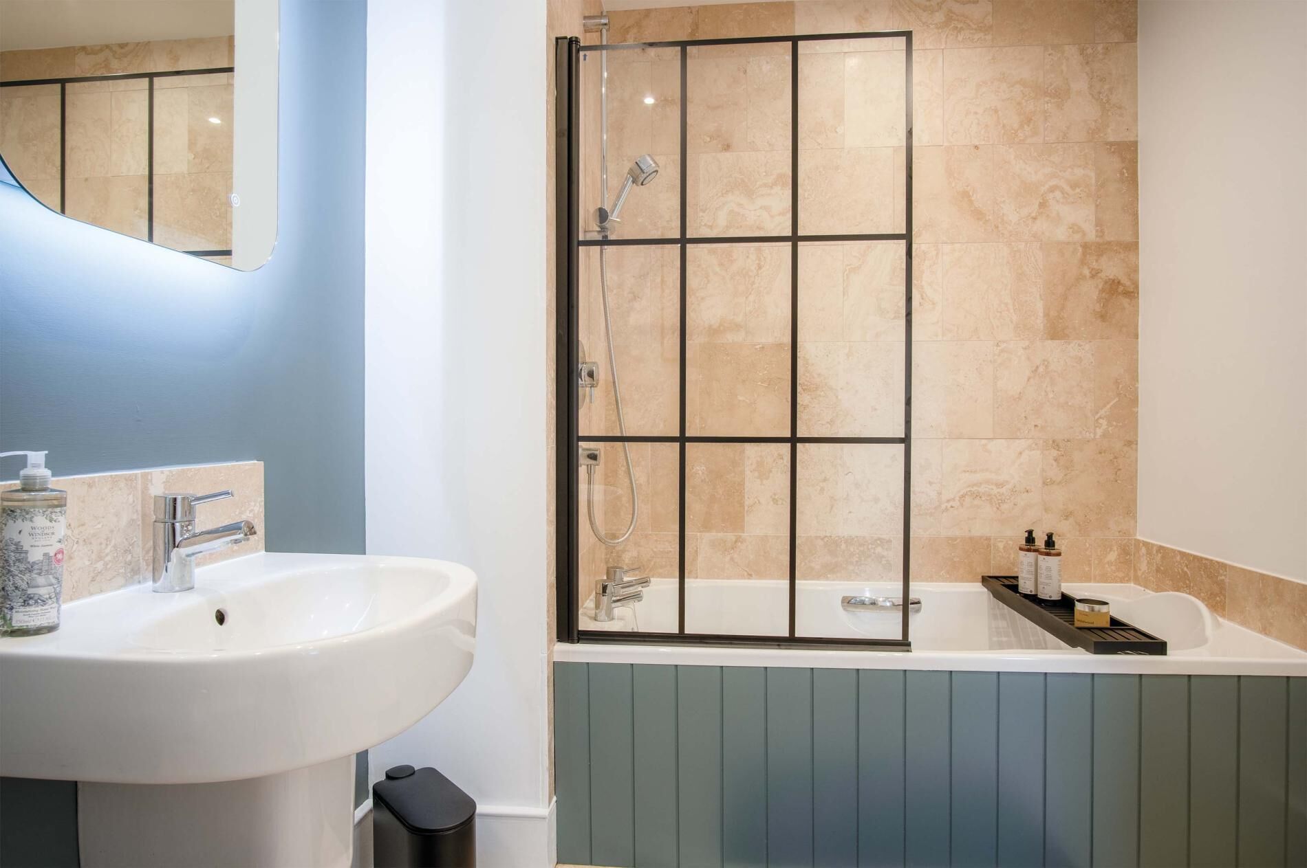 A bathroom with a white sink, a glass shower enclosure, and a bathtub with a wooden shelf.