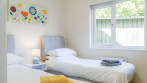 Une chambre d’hôtel avec deux lits, une table de chevet avec une lampe, une fenêtre donnant sur un paysage verdoyant et une œuvre d’art murale.