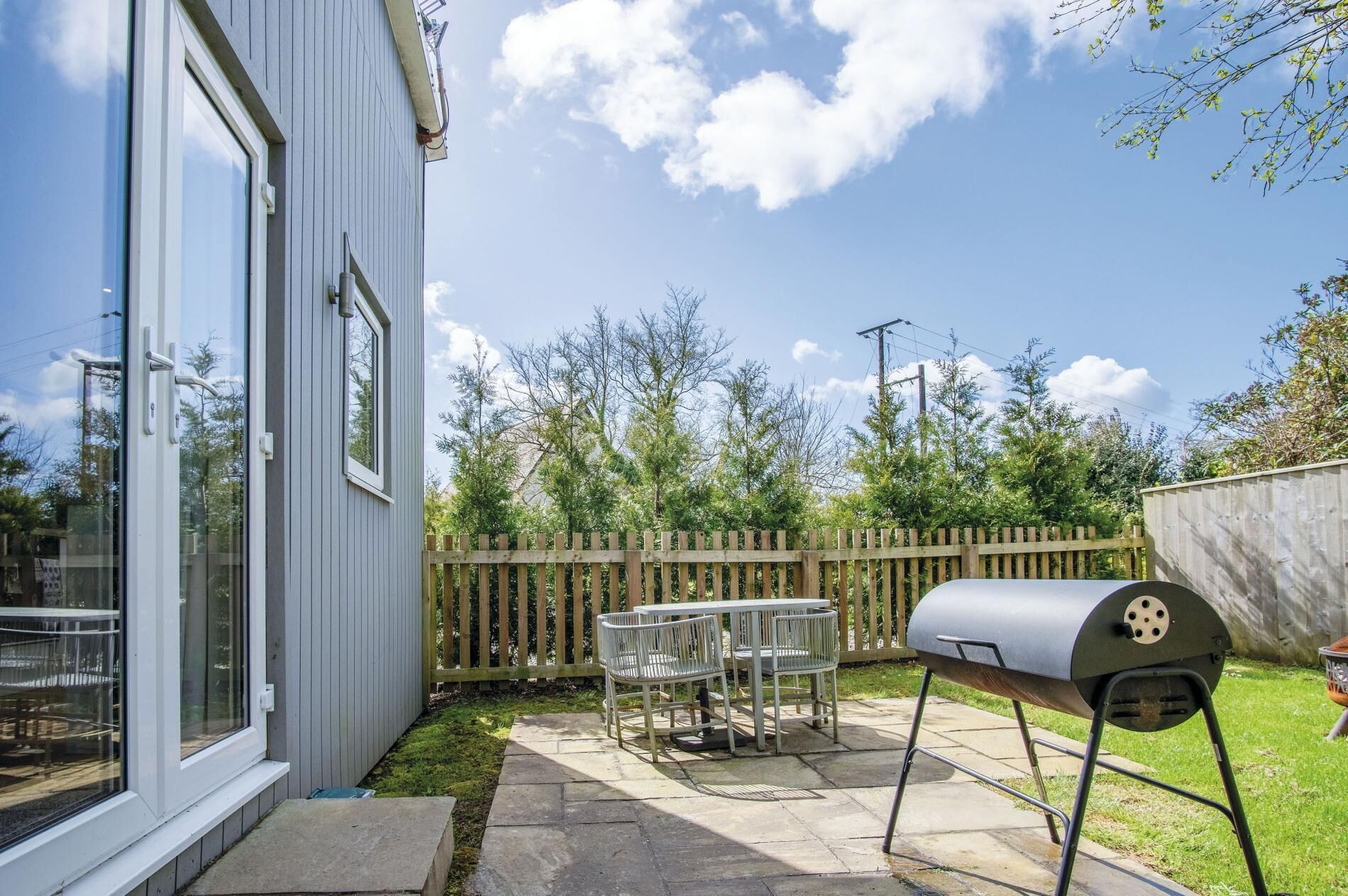 A backyard with a barbecue grill, a wooden fence, and a patio with outdoor furniture.
