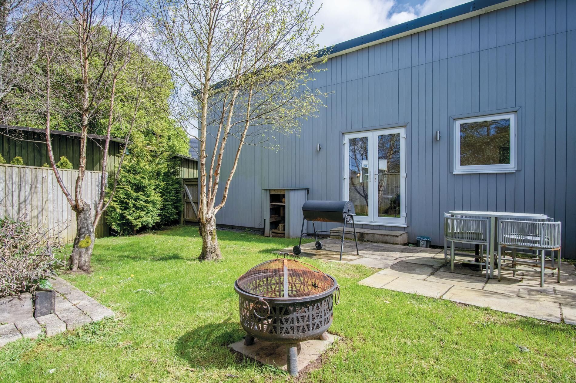 A backyard with a barbecue grill, a fire pit, a table and chairs, and a wooden fence.