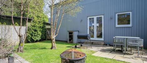 A backyard with a barbecue grill, a fire pit, a table and chairs, and a wooden fence.