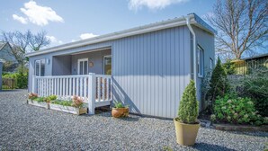 Une petite maison mobile d’un seul étage, dotée d’une véranda blanche et de plantes en pot.