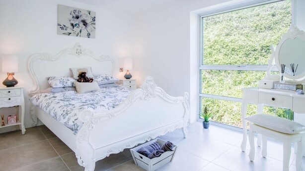 A bedroom with a large bed, a nightstand, a dresser, and a window with a view of greenery.