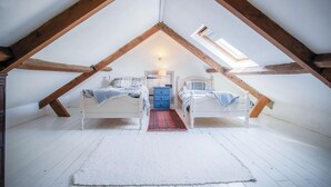 A bedroom with two beds, a blue dresser, a white rug, and a skylight. - Haggard - 3 Bedroom Cottage - Manorbier (Tenby)
